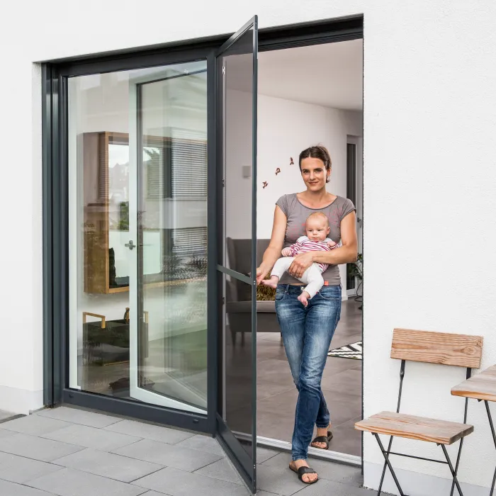 Hund steht vor geöffneter Fliegengitter Tür mit weißem Rahmen in einem hellen Wohnzimmer