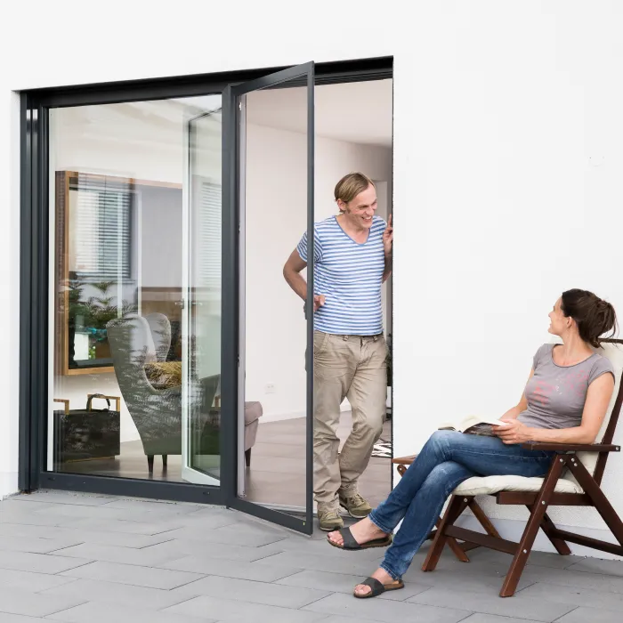 Mann grillt vor der geöffneten Fliegengitter Schiebetür mit weißem Rahmen am Haus