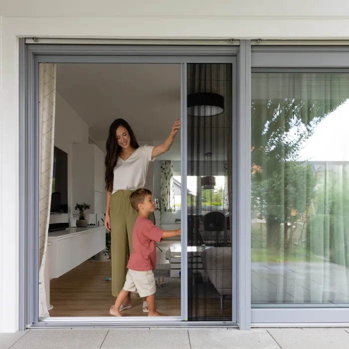 Frau und Kind an einer geöffneten Schiebetür mit integriertem Fliegengitter in einem modernen Haus mit Blick in den Garten