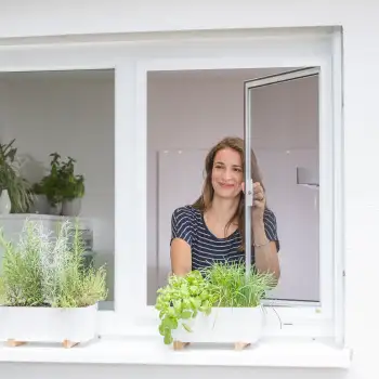 Frau ffnet Fenster mit integriertem Drehfenster Spannrahmen hinter Kchenkrutern