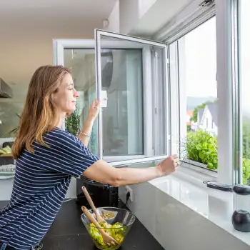 Frau ffnet Fenster mit eingesetztem Drehfenster Spannrahmen in der Kche