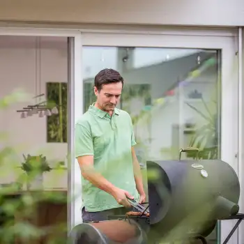 Mann grillt vor der geffneten Fliegengitter Schiebetr mit weiem Rahmen am Haus